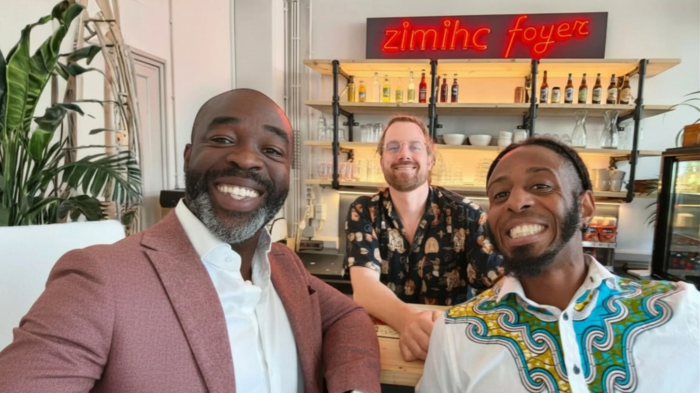 Drie mensen lachen in de foyer van ZIMIHC, met de neonletters zimihc foyer boven de bar